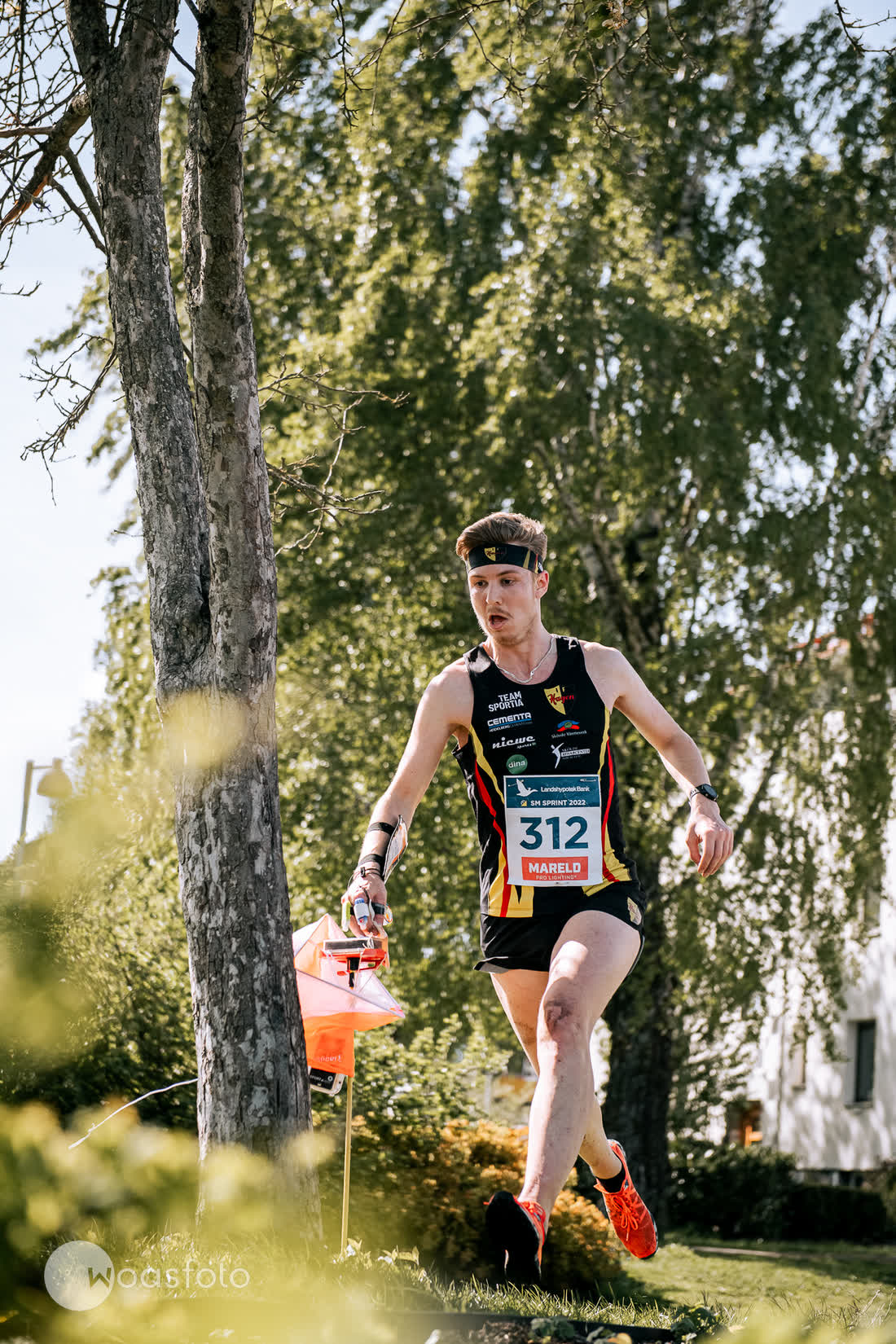 A sprint orienteer passing an orange control flag between apartment blocks